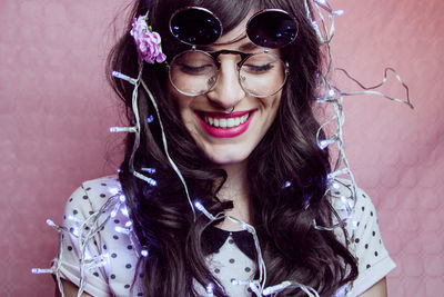 Smiling young woman with string light against wall