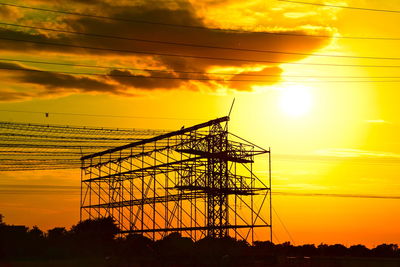 Low angle view of silhouette electricity pylon against orange sky