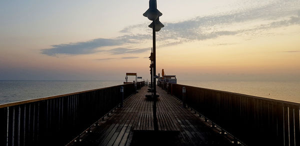 Street light on pier by sea against sky during sunset
