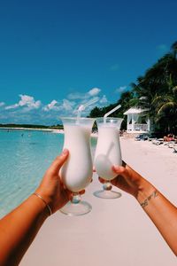 Cropped hands of friends toasting drinks at beach