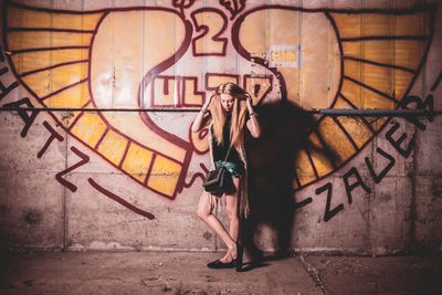 Beautiful young woman standing against graffiti wall