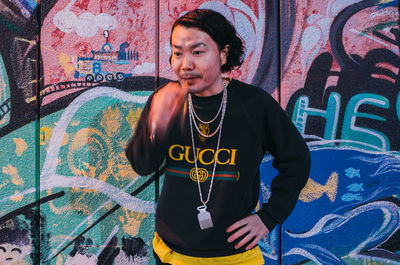 Full length of young man standing against graffiti wall