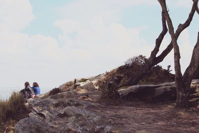 Friends sitting on shore against sky