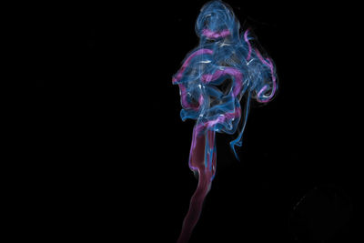 Close-up of multi colored illuminated smoke against black background