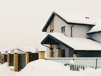 Snow covered houses by building against sky