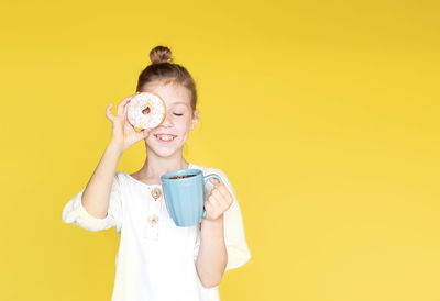 Portrait of young woman holding toy against yellow background