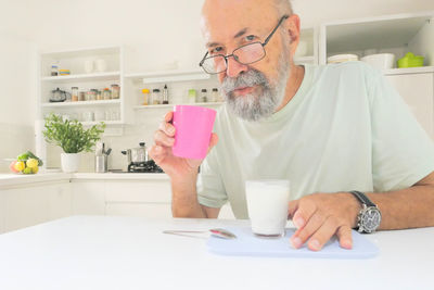 Senior man eating yogurt in the kitchen 
