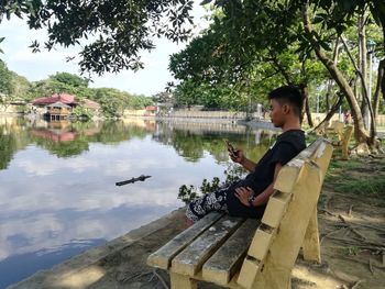 Side view of man sitting on lake against trees