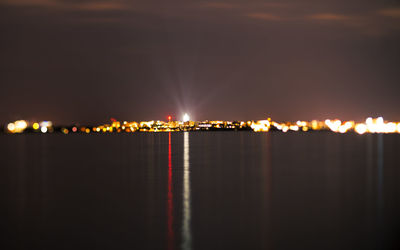 Illuminated city by sea against sky at night