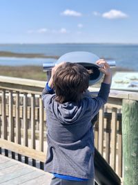 Rear view of boy standing by railing against sea