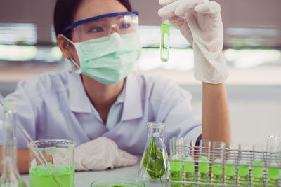 Scientist holding and looking at test tube with green liquid