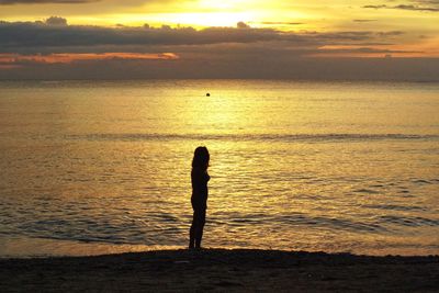 Silhouette woman standing on shore at beach during sunset