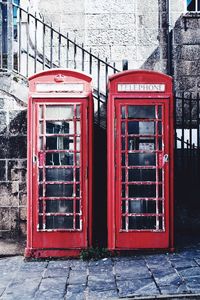 Red telephone booth on sidewalk by buildings in city