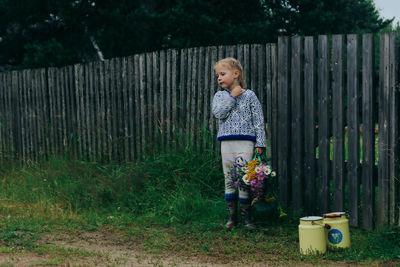 Girl standing by fence against plants in yard