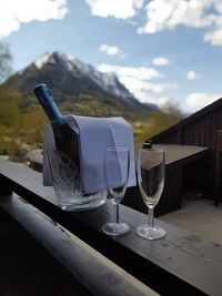 Champagne flutes by bottle on retaining wall against mountain