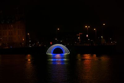 Illuminated bridge over river by buildings against sky at night