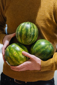 Unrecognizable male carrying small ripe watermelons on sunny day on market