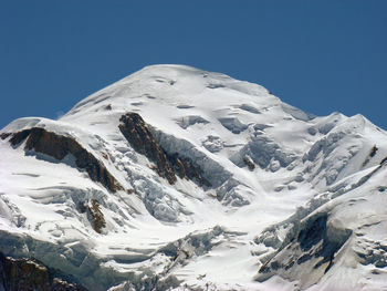 Low angle view of snowcapped mountains against clear blue sky