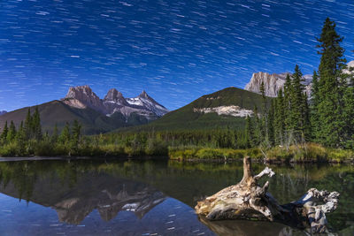 Three sisters trio peaks at night, starry sky reflected in the creek water surface. canadian rockies