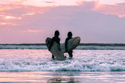 People on sea shore against sky during sunset