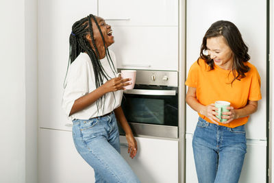 Young women holding coffee cup while standing at home