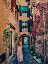 Rear view of woman standing on alley amidst buildings
