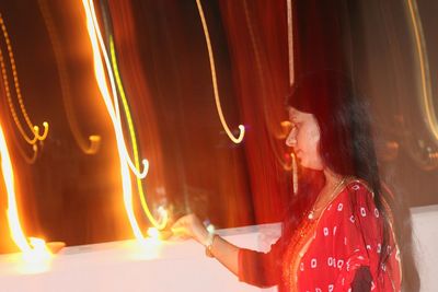 Woman igniting diya on retaining wall during diwali at night