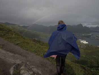 Rear view of man hiking on mountain against cloudy sky