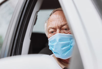 Senior man wearing mask sitting in car