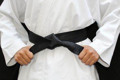 Midsection of athlete wearing black belt against black background