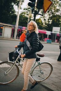 Senior woman with bicycle crossing road in city