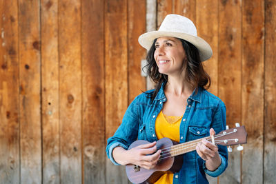 Smiling woman holding ukulele against wall