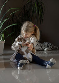 A little girl sits on the floor and holds a cat in her hands