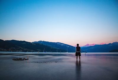 Rear view of man standing in lake against clear sky during dusk