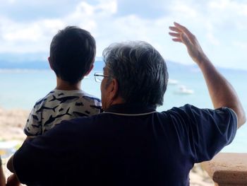 Rear view of grandfather carrying grandson against cloudy sky