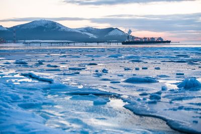 Scenic view of sea by snowcapped mountains against sky