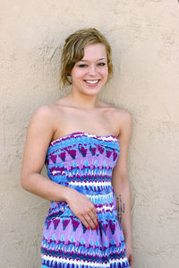 Portrait of smiling young woman standing against wall