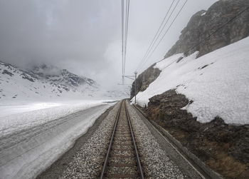 Railroad tracks by snow capped mountain against sky
