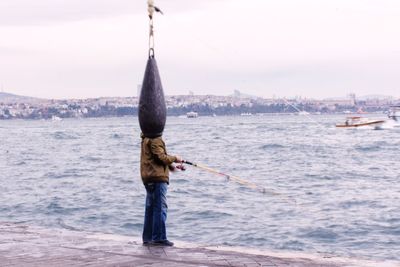 Rear view of man fishing in sea against sky