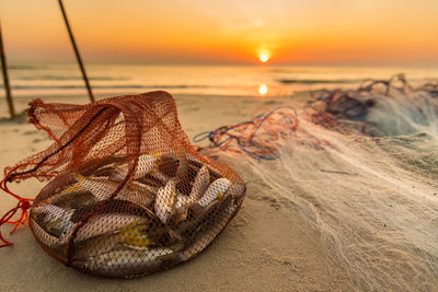 Close-up of fishing nets on beach against sky during sunset