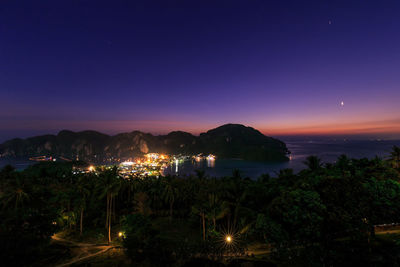 High angle view of illuminated city by sea at night