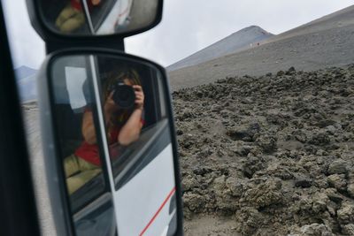 Reflection of man on side-view mirror of car