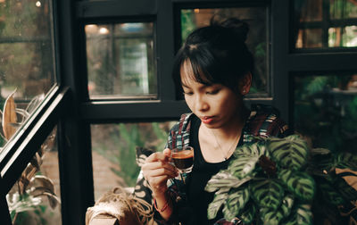 Young woman drinking glass from window