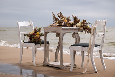 Chairs and table at beach by sea against sky