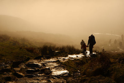 Rear view of people walking on mountain against sky