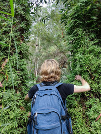 Woman with a camping backpack makes her way through the thicket, back view