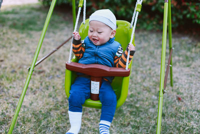 Cute baby boy sitting in swing at playground