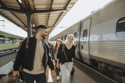 Smiling man walking with family near train at railroad station