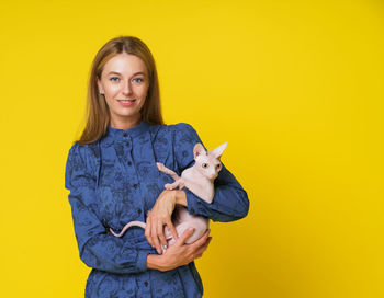 Portrait of young woman holding stuffed toy against yellow background