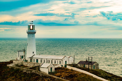 Lighthouse amidst sea and buildings against sky